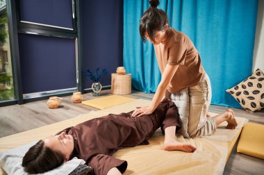 Masör Tayland yogası masajı yapıyor. Geleneksel masaj tedavisi uygulayan kadın terapist, kadın hastaların vücudunu geriyor. Müşteri paspasın üzerinde uzanıyor, sakin atmosferde el masajının keyfini çıkarıyor..