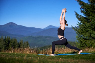 Dağlarda yoga yapan bir kadın, sakin, doğal bir ortamda. Kadın yoga pozu veriyor paspasın üzerinde, gün doğumunda ya da günbatımında güzel dağ manzarasının arka planıyla.