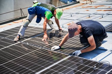 İşçiler evin metal çatısında güneş paneli inşa ediyorlar. İki adam dışarı fotovoltaik güneş modülü kuruyor. Alternatif, yeşil ve yenilenebilir enerji üretimi kavramı.