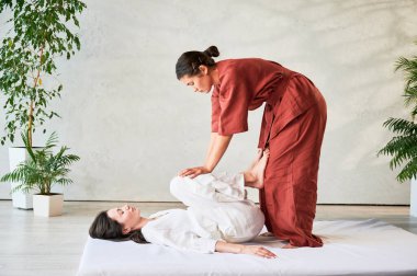 Masör Tayland yogası masajı yapıyor. Geleneksel masaj tedavisi uygulayan kadın terapist, kadın hastaların vücudunu geriyor. Müşteri paspasın üzerinde uzanıyor, sakin atmosferde el masajının keyfini çıkarıyor..