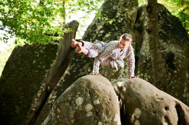 Ormanda yoga yapan bir kadın. Yoga minderinde çıplak ayaklı kadın. Etrafı ağaçlar ve kayalarla çevrili. Bu da meditasyon ya da yoga için ideal barışçıl, doğal bir ortam olduğunu gösteriyor..