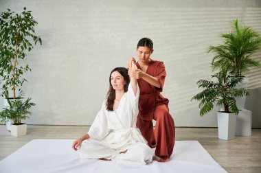 Masör Tayland yogası masajı yapıyor. Kadın terapist, kadın hasta için evde geleneksel masaj tedavisi uyguluyor. Müşteri mindere oturuyor, meditasyon yapıyor, sakin bir atmosferde el masajının keyfini çıkarıyor..