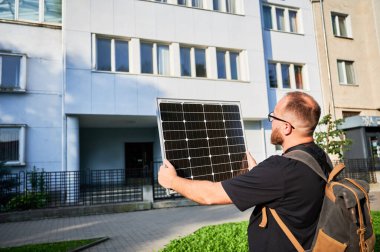 Tarihsel binanın önünde fotovoltaik güneş paneli tutan adam. Sürdürülebilir yenilenebilir enerji kaynaklarının mimariye entegrasyonu kavramı.