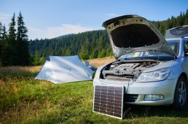 Kaputu açık arabanın önündeki güneş paneli geleneksel içten yanmalı motorlardan elektrikli arabalara geçişi sembolize ediyor. Kablo, güneş panelini yenilenebilir enerji kullanımına bağlıyor