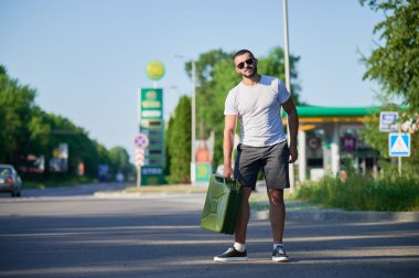 Kendine güvenen adam sonunda benzin istasyonunu buldu ve teneke kutuyu doldurdu. Adam yakıt ikmali için arabaya dönüyor. Benzin istasyonunun arka planında elinde teneke kutuyla genç bir erkek..