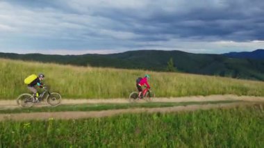 Dışarıda bisiklete binen iki bisikletçi. Erkek turistler dağlarda bisiklet sürüyorlar, kaskları ve sırt çantaları takıyorlar. Spor anlayışı, aktif eğlence ve doğa.