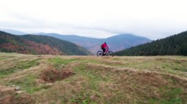 Dışarıda elektrikli dağ bisikleti süren bisikletçi. Erkek turistin dağlardaki otlak patika boyunca bisiklet sürüşünü, kaskını ve sırt çantasını gösteren hava manzarası. Spor anlayışı, aktif eğlence ve doğa.