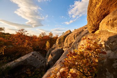 Golden hues of setting sun illuminate rocky formations and autumn foliage, casting warm glow on scene. Vibrant oranges and reds of trees below. Dovbush Rocks, Carpathian mountains, Ukraine, Europe. clipart