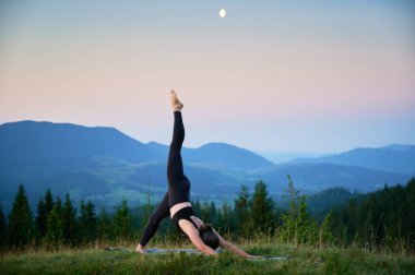 Dağlarda yoga yapan bir kadın, sakin, doğal bir ortamda. Yoga yapan kadın, gün doğumunda ya da günbatımında güzel dağ manzarasının arkaplanıyla.