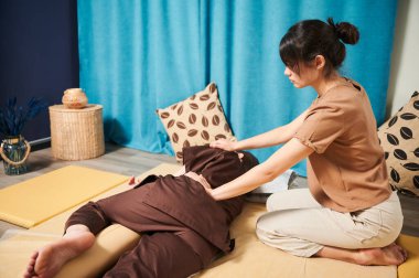 Masör Tayland yogası masajı yapıyor. Kadın terapist, kadın hasta için evde geleneksel masaj tedavisi uyguluyor. Müşteri paspasın üzerinde uzanıyor, meditasyon yapıyor, sakin bir atmosferde el masajının keyfini çıkarıyor..