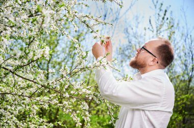 Alerjisi olan bir adam bahar mevsimsel alerjisinden zevk alıyor. Baharda çiçek açan ağacın önünde gülümseyen mutlu sakallı adamın portresi. Bahar alerjisi konsepti.