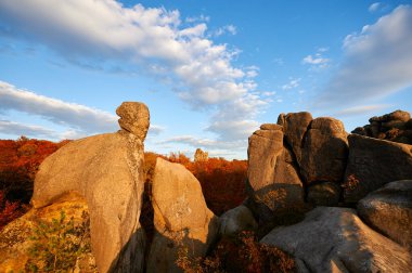 Dramatik kaya oluşumları, sonbahar yaprakları ve parlak mavi gökyüzünün arka planına karşı dimdik ayakta duruyor. Batan güneşin sıcacık ışığı uzun gölgeler bırakır. Dovbush Kayaları, Karpat Dağları, Ukrayna.