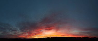 Göz kamaştırıcı günbatımı gökyüzünü kırmızı, turuncu ve pembe renkleriyle boyar. Derin maviler ve morlar ile harmanlanır. Siluetli tepeler, ateşli ufka karşı tezat oluşturarak, huzurlu manzaraya dram katıyor..