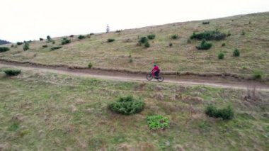 Dışarıda elektrikli dağ bisikleti süren bisikletçi. Erkek turistin dağlardaki otlak patika boyunca bisiklet sürüşünü, kaskını ve sırt çantasını gösteren hava manzarası. Spor anlayışı, aktif eğlence ve doğa.