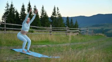 Dağlarda yoga yapan bir kadın, sakin, doğal bir ortamda. Mavi hasırda yoga yapan kadın, gün doğumunda ya da günbatımında güzel dağ manzarasının arkaplanıyla.