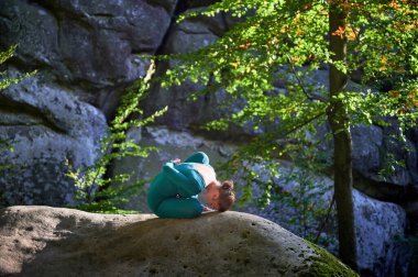 Ormanda yoga yapan bir kadın. Yoga minderinde çıplak ayaklı kadın. Etrafı ağaçlar ve kayalarla çevrili. Bu da meditasyon ya da yoga için ideal barışçıl, doğal bir ortam olduğunu gösteriyor..