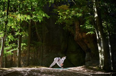 Ormanda yoga yapan bir kadın. Yoga minderinde çıplak ayaklı kadın. Etrafı ağaçlar ve kayalarla çevrili. Bu da meditasyon ya da yoga için ideal barışçıl, doğal bir ortam olduğunu gösteriyor..