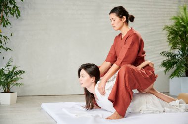 Masör Tayland yogası masajı yapıyor. Geleneksel masaj tedavisi uygulayan kadın terapist, kadın hastaların vücudunu geriyor. Müşteri paspasın üzerinde uzanıyor, sakin atmosferde el masajının keyfini çıkarıyor..