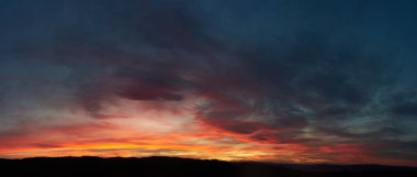 Göz kamaştırıcı günbatımı gökyüzünü kırmızı, turuncu ve pembe renkleriyle boyar. Derin maviler ve morlar ile harmanlanır. Siluetli tepeler, ateşli ufka karşı tezat oluşturarak, huzurlu manzaraya dram katıyor..