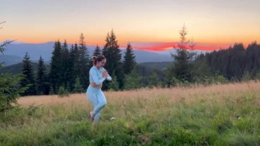 Dağlarda yoga yapan bir kadın, sakin, doğal bir ortamda. Kadın yoga pozu veriyor paspasın üzerinde, gün doğumunda ya da günbatımında güzel dağ manzarasının arka planıyla.