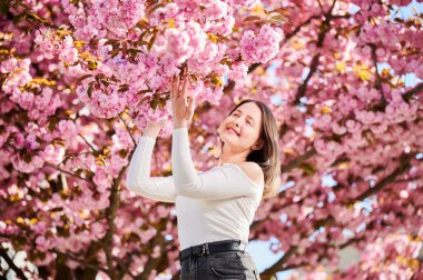 Alerjisi olan bir kadın, bahardaki sezonluk alerjiden zevk alıyor. Baharda çiçek açan sakura ağacının önünde gülümseyen güzel bir kadının portresi. Bahar alerjisi konsepti.