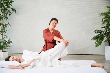 Masör Tayland yogası masajı yapıyor. Geleneksel masaj tedavisi uygulayan kadın terapist, kadın hastaların vücudunu geriyor. Müşteri paspasın üzerinde uzanıyor, sakin atmosferde el masajının keyfini çıkarıyor..