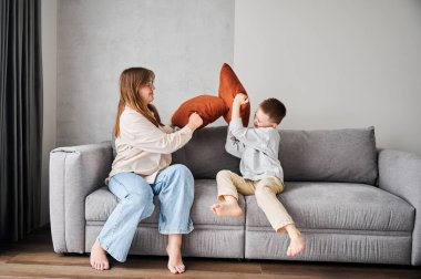 İki küçük kardeş kanepede yastık savaşı başlattı. Küçük oğlan ve ablası yastıklarla kavga ediyorlar. Aileyle evde eğlenceli vakit geçirmek.