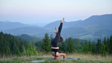 Yoga yapan ve dışarıda, dağlarda meditasyon yapan bir kadın, sakin, doğal bir ortamda. Kadın yoga pozu veriyor paspasın üzerinde, gün doğumunda ya da günbatımında güzel dağ manzarasının arka planıyla.