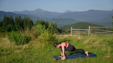 Dağlarda yoga yapan bir kadın, sakin, doğal bir ortamda. Kadın yoga pozu veriyor paspasın üzerinde, gün doğumunda ya da günbatımında güzel dağ manzarasının arka planıyla.