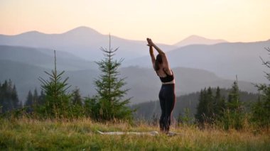 Dağlarda yoga yapan bir kadın, sakin, doğal bir ortamda. Kadın yoga pozu veriyor paspasın üzerinde, gün doğumunda ya da günbatımında güzel dağ manzarasının arka planıyla.