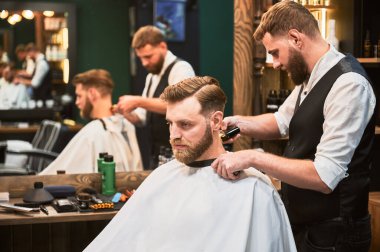 Profesyonel berber müşterilerin ensesini tıraş ediyor. Sakallı yakışıklı müşteri şık saç tıraşı oluyor. Kendine güveni tam bir adam berber dükkanına düzenli olarak gelir..