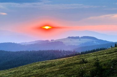 Güneş siluetli dağların ardında batar, sıcak, altın renginde bir parıltı yayar gökyüzünde. Yumuşak bulutlar, pembe ve turuncu renklerle karıncalanmış, tembelce sürükleniyor, dingin ve sakin bir akşam sahnesi yaratıyor..