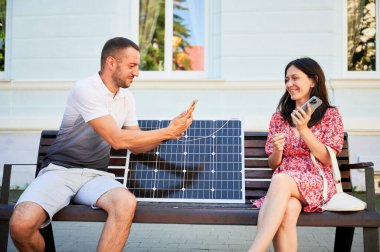 Gülümseyen kadın kocasına güneş pilinin nasıl kullanılacağını gösteriyor. Mobil cihazları şarj etmek için taşınabilir güneş paneli kullanan sevimli bir çift. Alternatif enerji kaynakları kavramı.