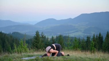 Dağlarda yoga yapan bir kadın, sakin, doğal bir ortamda. Kadın yoga pozu veriyor paspasın üzerinde, gün doğumunda ya da günbatımında güzel dağ manzarasının arka planıyla.