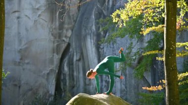 Ormanda yoga yapan bir kadın. Yoga minderinde çıplak ayaklı kadın. Etrafı ağaçlar ve kayalarla çevrili. Bu da meditasyon ya da yoga için ideal barışçıl, doğal bir ortam olduğunu gösteriyor..