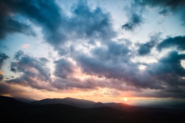 Ormanda hava manzarası nefes kesici gün batımı. Güneş ışınları dramatik bulutları delip geçiyor. Yuvarlanan tepeler ve vadiler boyunca altın parıltılar saçıyor. Uzak dağlar huzur ve resim manzarası yaratıyor..