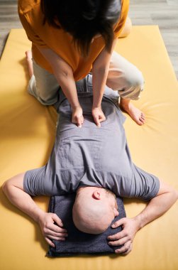 Masör Tayland yogası masajı yapıyor. Kadın terapist erkek hasta için evde geleneksel masaj tedavisi uyguluyor. Kel müşteri paspasın üzerinde uzanıyor, meditasyon yapıyor, sakin atmosferde el masajının keyfini çıkarıyor..