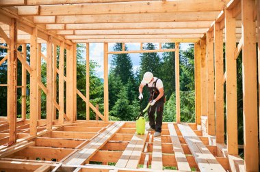 İşçi, ormanın yakınında ahşap çerçeve inşa ediyor. Adam odunları tedavi ediyor, yangın söndürücü sürüyor koruyucu giysi ve kask takıyor. Modern çevre dostu yapı kavramı.