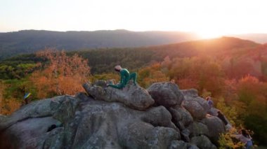 Yoga ve meditasyon yapan bir kadın akşamları dev bir kayanın tepesinde. Güzel günbatımı, sonbahar ormanları, arka planda kayalar ve tepeler. Hava aracı görünümü