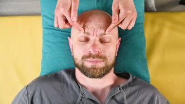 Tayland yüz masajı yaptıran adama yaklaş. Erkek hastaya geleneksel masaj yapan bir masöz. Kel bir müşteri, gözleri kapalı, meditasyon yapıyor, sakin bir atmosferde el masajının keyfini çıkarıyor..