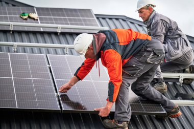 Evin çatısına fotovoltaik güneş panelleri kuran kurulumcular. Miğferli mühendisler, uğursuz anahtar yardımıyla güneş modülü sistemi inşa ediyorlar. Alternatif, yenilenebilir enerji kavramı.