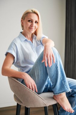 Bar taburesinde rahatlayan güzel bir kadın. Kameraya gülümseyen sarı saçlı kadın portresi. Evinde bar taburesinde oturan güzel bir kadın..