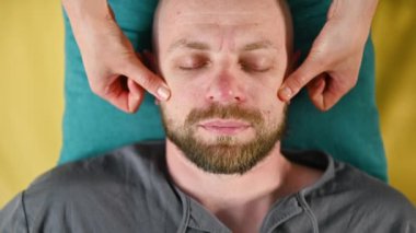 Tayland yüz masajı yaptıran adama yaklaş. Erkek hastaya geleneksel masaj yapan bir masöz. Kel bir müşteri, gözleri kapalı, meditasyon yapıyor, sakin bir atmosferde el masajının keyfini çıkarıyor..