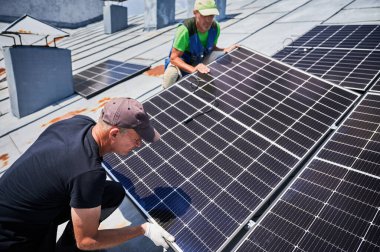 İşçiler evin metal çatısında güneş paneli inşa ediyorlar. İki adam dışarı fotovoltaik güneş modülü kuruyor. Alternatif, yeşil ve yenilenebilir enerji üretimi kavramı.