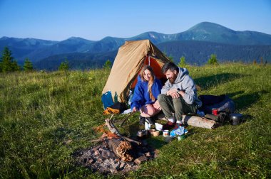Sabahları iki çadırı olan manzaralı dağ kampı. İki kampçı, bulutsuz gökyüzünün altında yuvarlanan dağların huzurlu manzarasının keyfini çıkarıyorlar. Resimli gündoğumu manzarası, huzurlu ve rahat bir açık hava deneyimi yaratıyor..