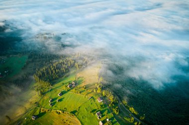 Sabah sisi ile kaplanmış yemyeşil vadinin hava manzarası, dağınık çiftlik evleri manzarayı noktalıyor. Sis mistik bir atmosfer yaratır, canlı alanları ve sık ormanları rüya sahnesine harmanlar..