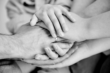 Sevimli bir aile el ele tutuşup birbirlerine yardım ve destek sözü veriyor. Aile üyelerinin destekleyici bir şekilde el ele tutuşmalarını yakından izleyin. Birlik ve takım çalışması kavramı. Siyah ve beyaz.