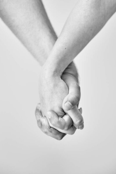 Two hands held together in grasp against neutral background. Close up of mans and womans hand. Concept of intimacy, support, and trust. Black and white image.