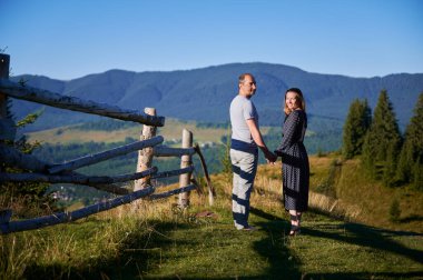Çiftler kırsal çitler boyunca el ele yürür. Kadın ve erkek çarpıcı dağ manzarasının tadını çıkarıyorlar. Açık mavi gökyüzü ve yemyeşil, huzurlu ve romantik bir ortam yaratır..
