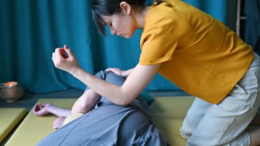 Masseuse making thai yoga massage. Woman therapist doing traditional massage treatment using elbow for male patient indoors. Client lying on mat, meditating, enjoying hand massage in calm atmosphere.